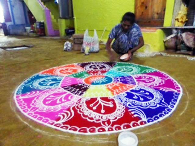 A woman creating a colourful rangoli mandala on the ground by hand